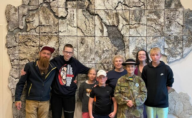 Kopbilde ar jaunejiem reindžeriem un skolotājiem pie mākslas objekta.