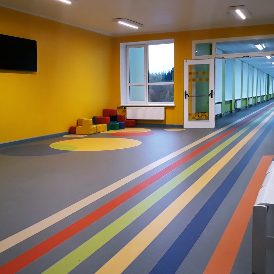 Skolas otrā stāva koridoris ar televizoru un krāsainiem apzīmējumiem, kas ved uz klasēm.