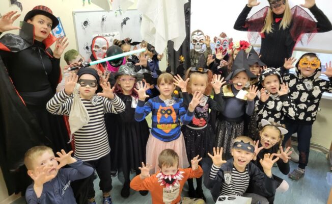 Mazo ģimnāzistu un audzinātāju kopbilde Helovīnu tērpos. Mazie ģimnāzisti un audzinātāji rāda draudzīgi biedējošas sejas.