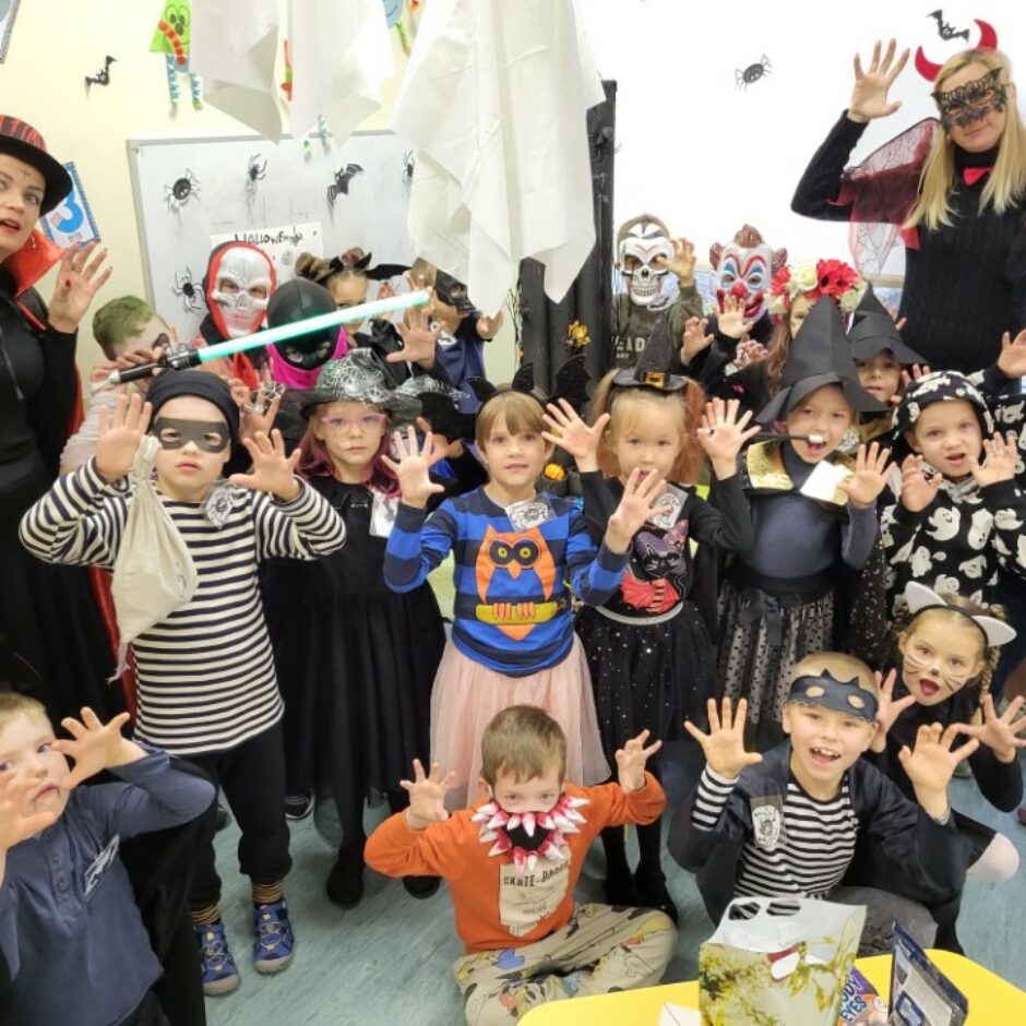 Mazo ģimnāzistu un audzinātāju kopbilde Helovīnu tērpos. Mazie ģimnāzisti un audzinātāji rāda draudzīgi biedējošas sejas.