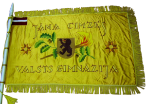Skolas karoga averss ar tekstu "Valkas Jāņa Cimzes ģimnāzija", Latvijas karogs kreisajā augšējā stūrī, centrā ģērbonis - lācis, fons dzeltenā krāsā.